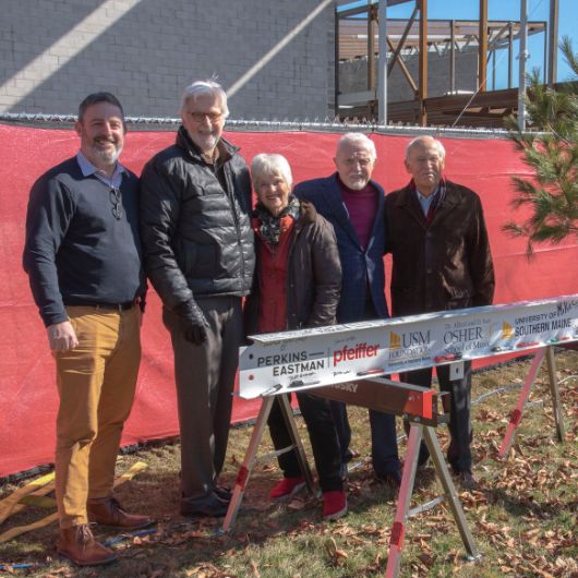 Gathered beside the Crewe Center’s last structural beam (from left) are Dean Adam Tuchinsky, Tom Chappell, Kate Cheney Chappell, Dan Crewe, and Peter Plumb.