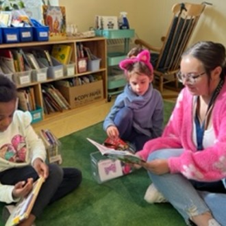 Westbrook High School student Makayla Morello looks at a book with two students in an elementary school classroom
