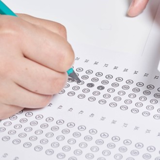 Student hand holding a pencil filling out a scantron or bubble sheet