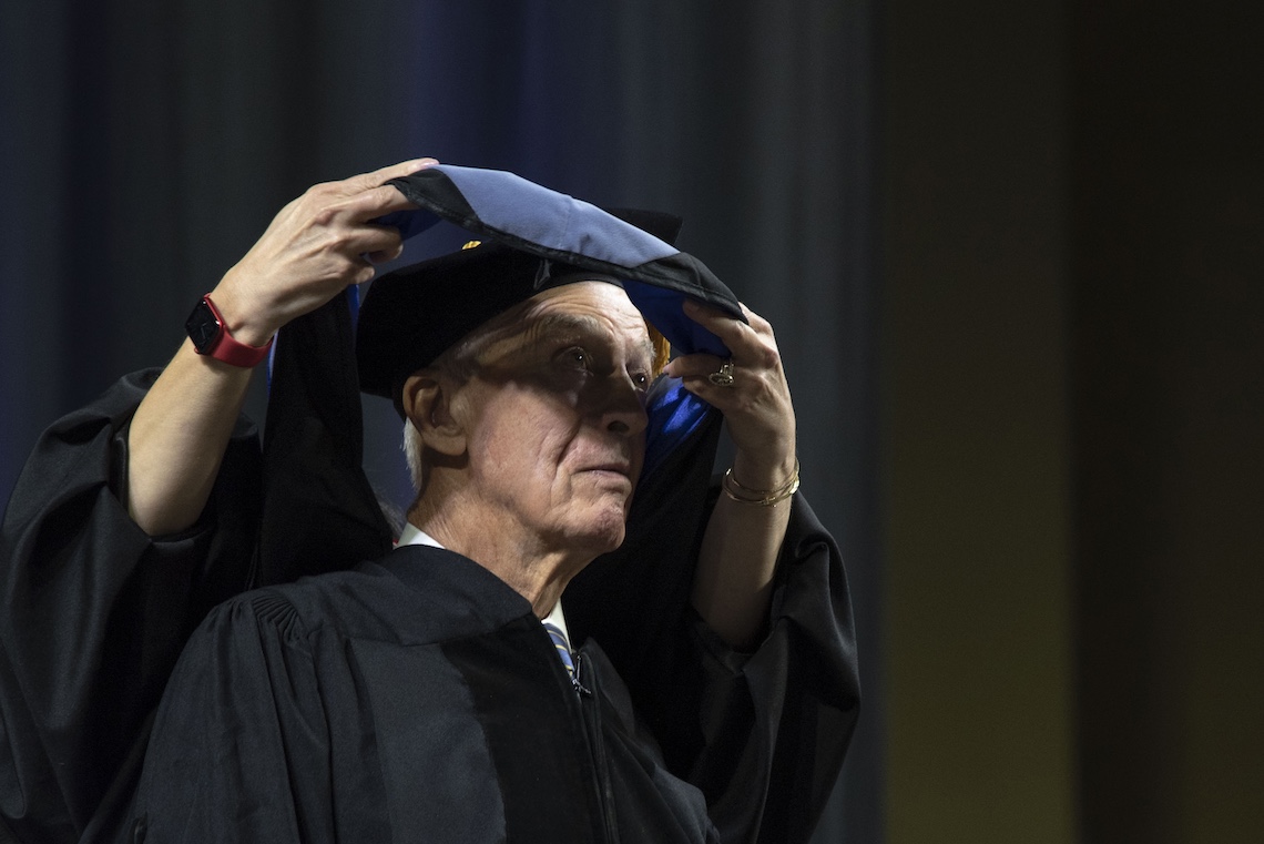 Joe Wishcamper receives a traditional hood to signify the honorary degree he received at the 2024 Commencement ceremony.