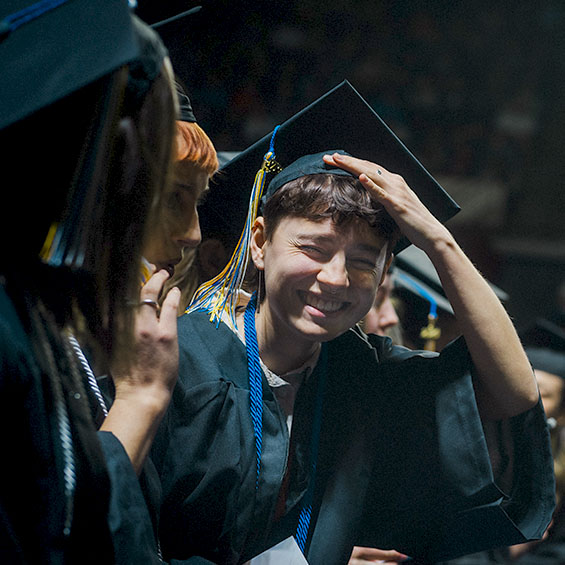 A student laughs while adjusting their graduation cap at Commencement.