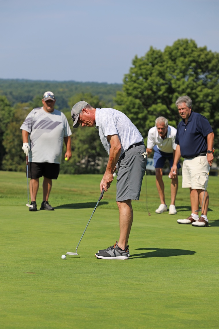 As a golfer lines up his putt, the rest of his team watches intently at the 2024 Husky Golf Classic.