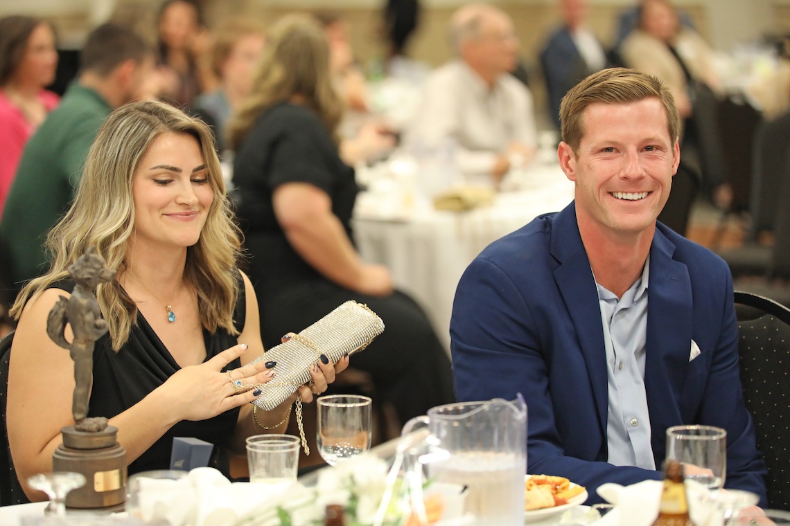 Nicole Kirk takes a seat next to proud husband Jamie Ruginski after delivering her acceptance speech at the 2024 Husky Hall of Fame induction ceremony.