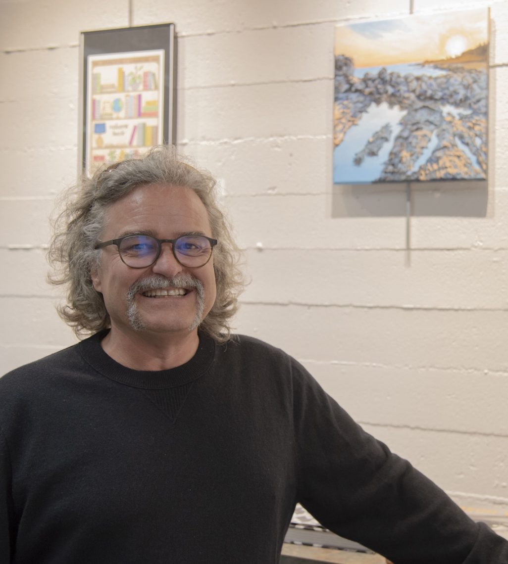 Greg Daly smiles beside his acrylic painting "Higgins" at the Employee Art Exhibition.