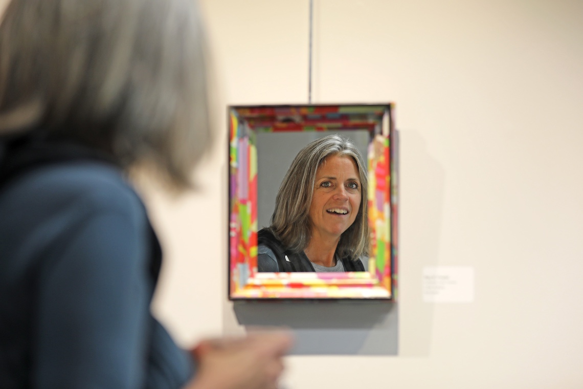 The mirrored surface of "I Am Vulture" by Roy K. Fowler catches the reflection of a visitor to the Employee Art Exhibition.