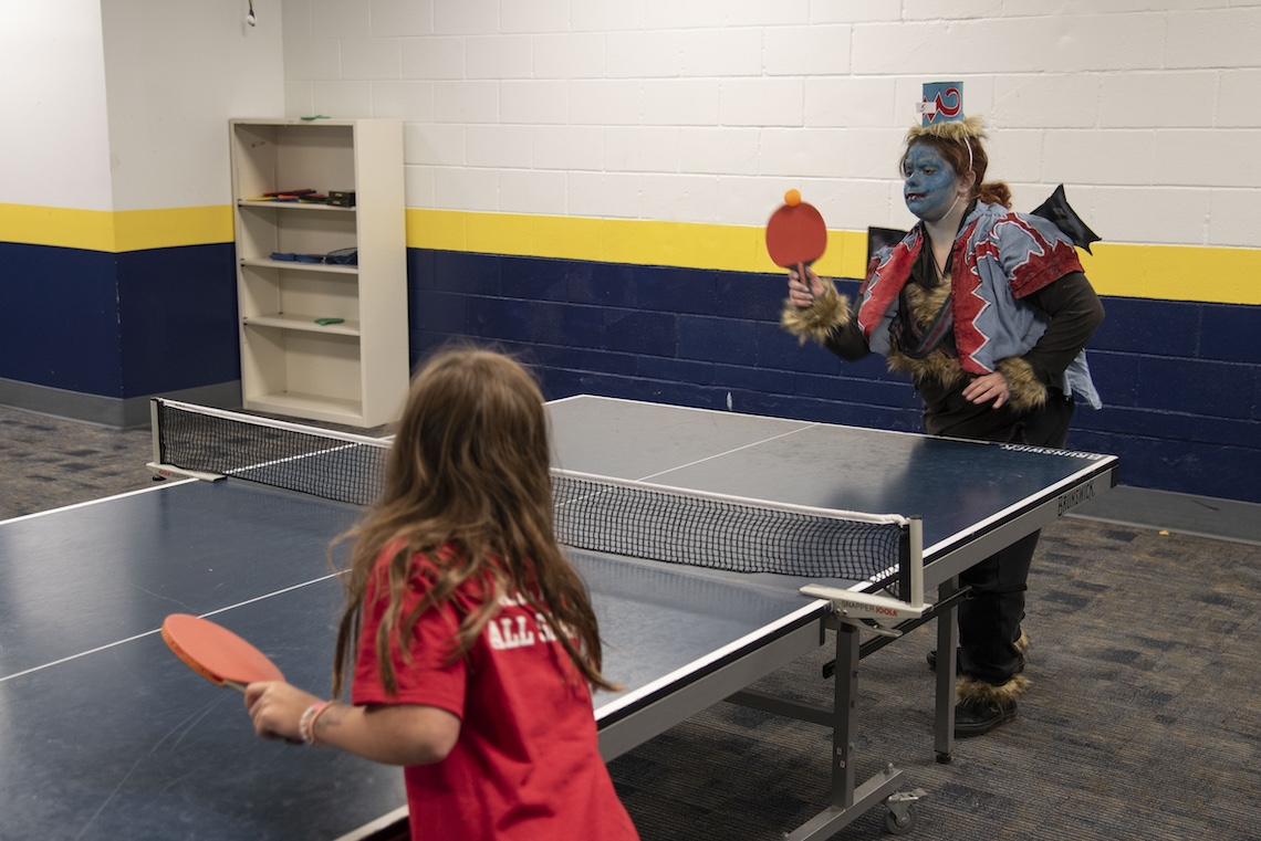 A guest at the listening party for "The Wizard of Oz" radio show kills time before the broadcast begins by playing ping-pong while dressed as a flying monkey.