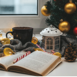 Open book with a candy cane bookmark next to a pine tree, candle and mug