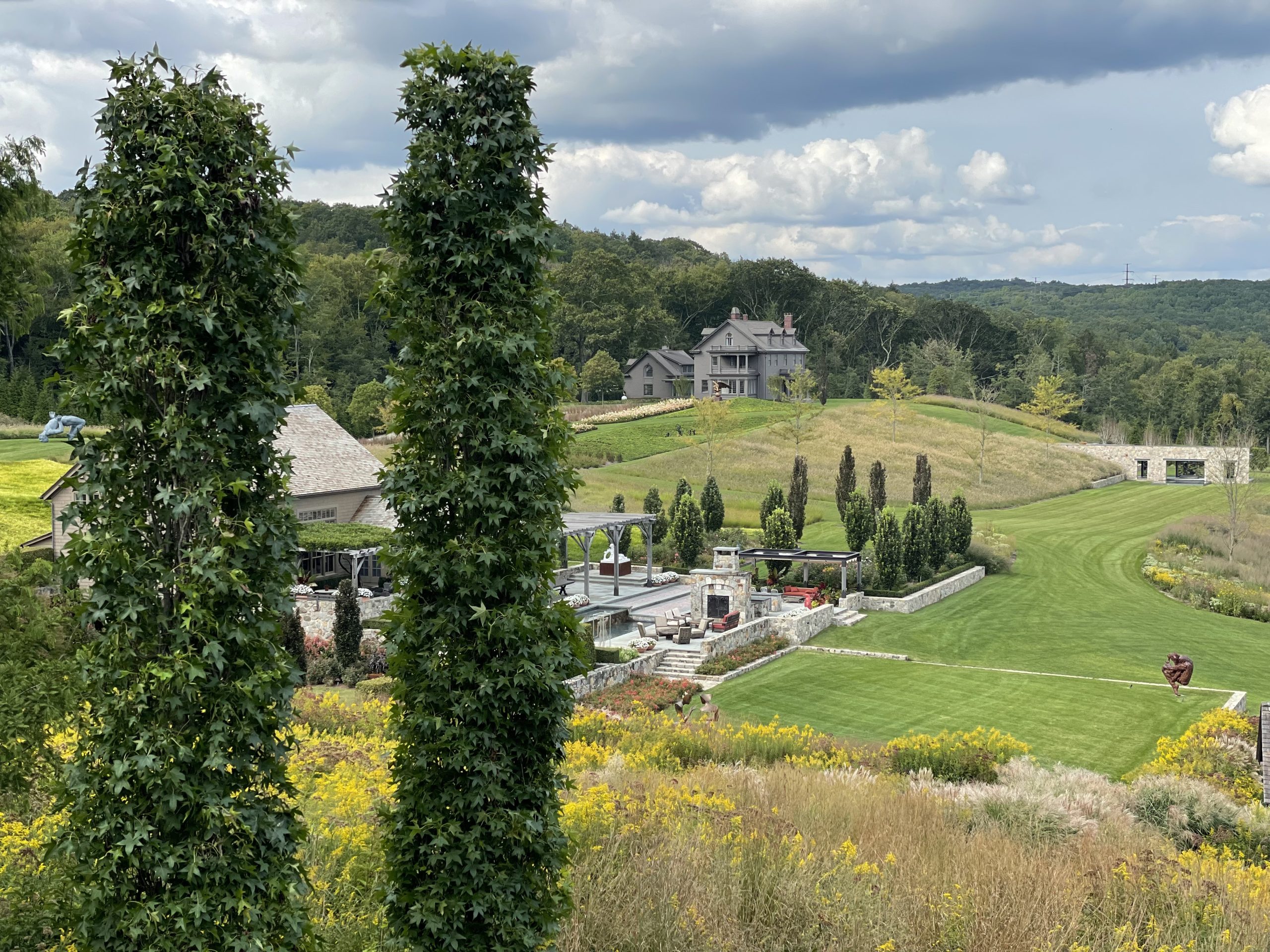 Shot of inSitu landscape from a distance, with trees and retreat buildings in foreground and house and hills in background