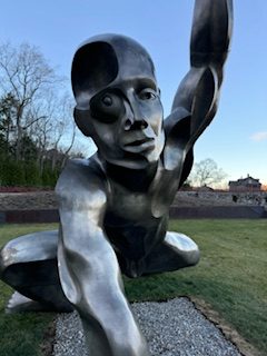 Large metal sculpture of figure on ground reaching arm forward