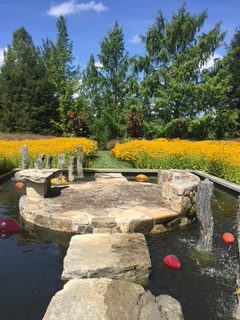 landscape image of inSitu sculpture garden with yellow flowers in background and stone sitting area in foreground