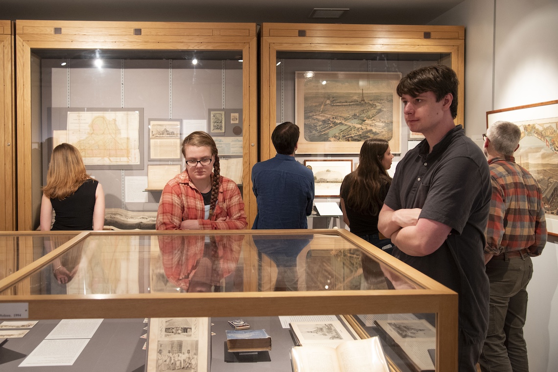 The exhibition of "A World On Display" includes photos, maps, and promotional art, as well as bulkier objects like painted dishware and a decorative clock.