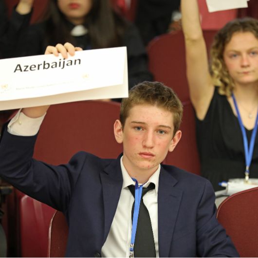 Delegates at the 2025 Maine Model United Nations Conference vote by raising the placards upon which the names of their countries are printed.