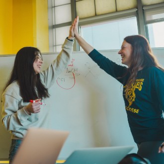 Two students high fiving in front of a whiteboard