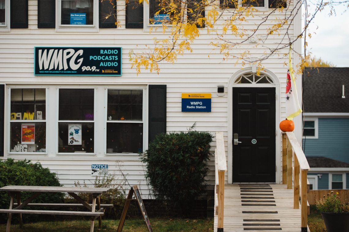Exterior of the WMPG building on the University of Southern Maine campus, featuring a sign that reads “WMPG Radio Podcasts Audio 90.9 University of Southern Maine.”