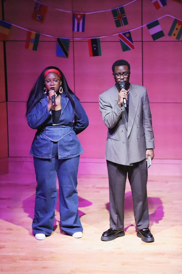 Two performers stand and speak into the microphone onstage at Afrochella