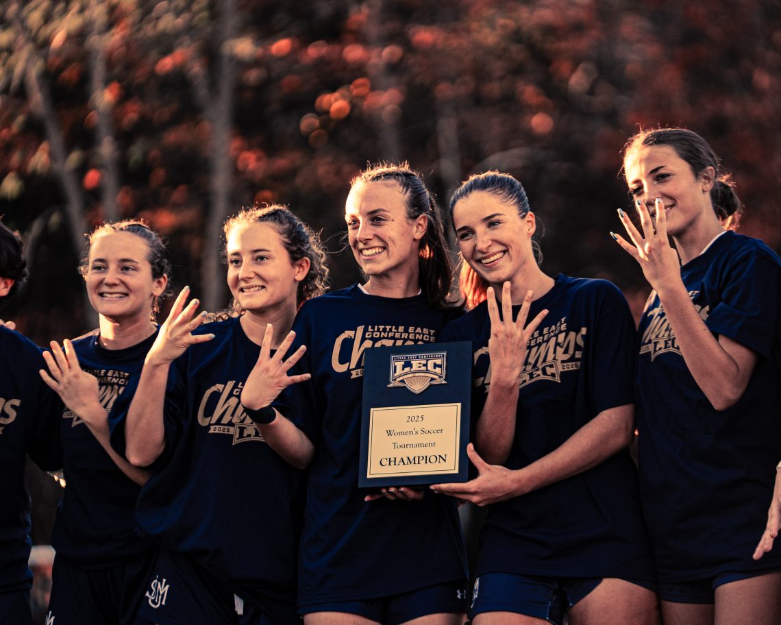USM Women's soccer team players hold LEC championship title in 2024, putting up 4 fingers for four years of winning the championship.