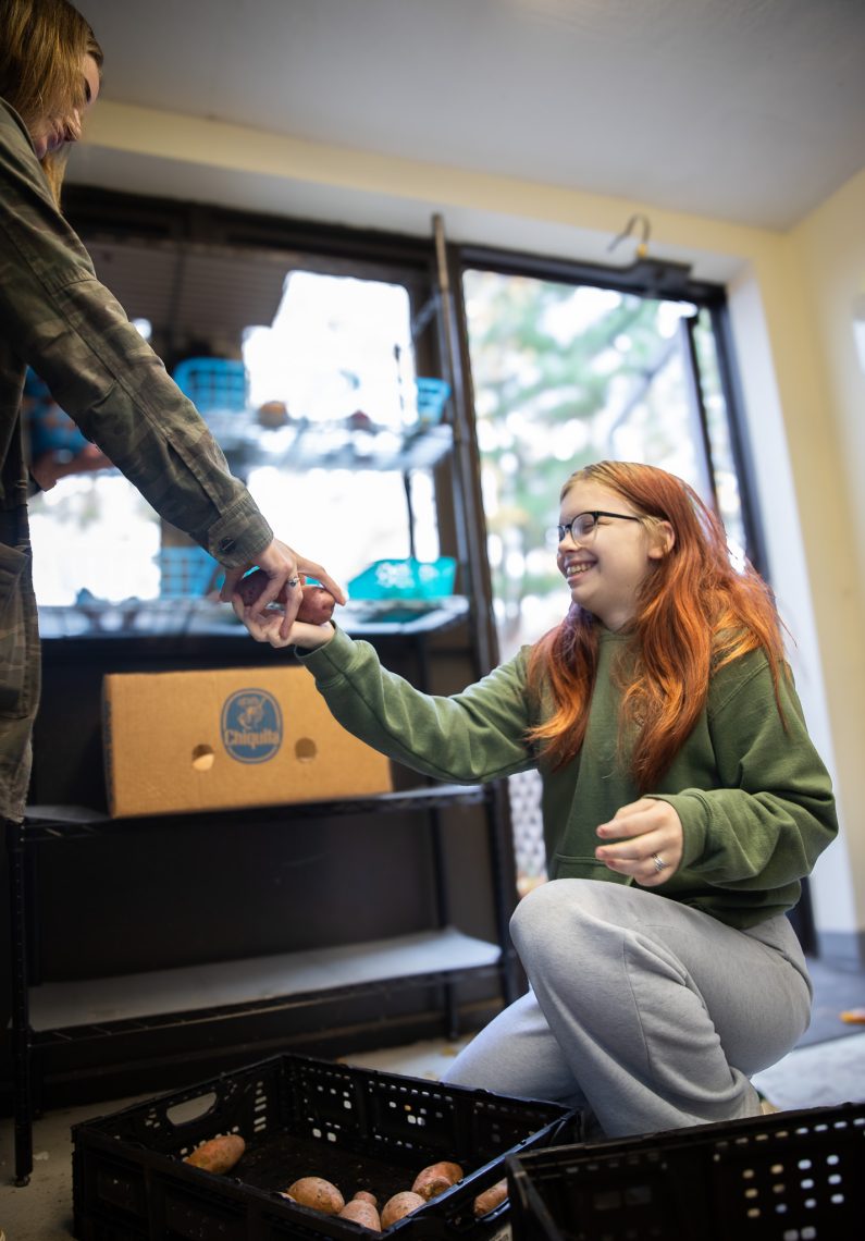 Student worker helps Sarah Farrugia stock Oakhurst Food Pantry shelves with potatoes.