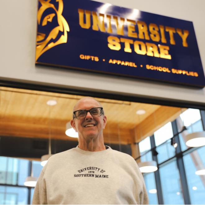 Vernon Tarbell poses outside USM's University Store with sign in the background