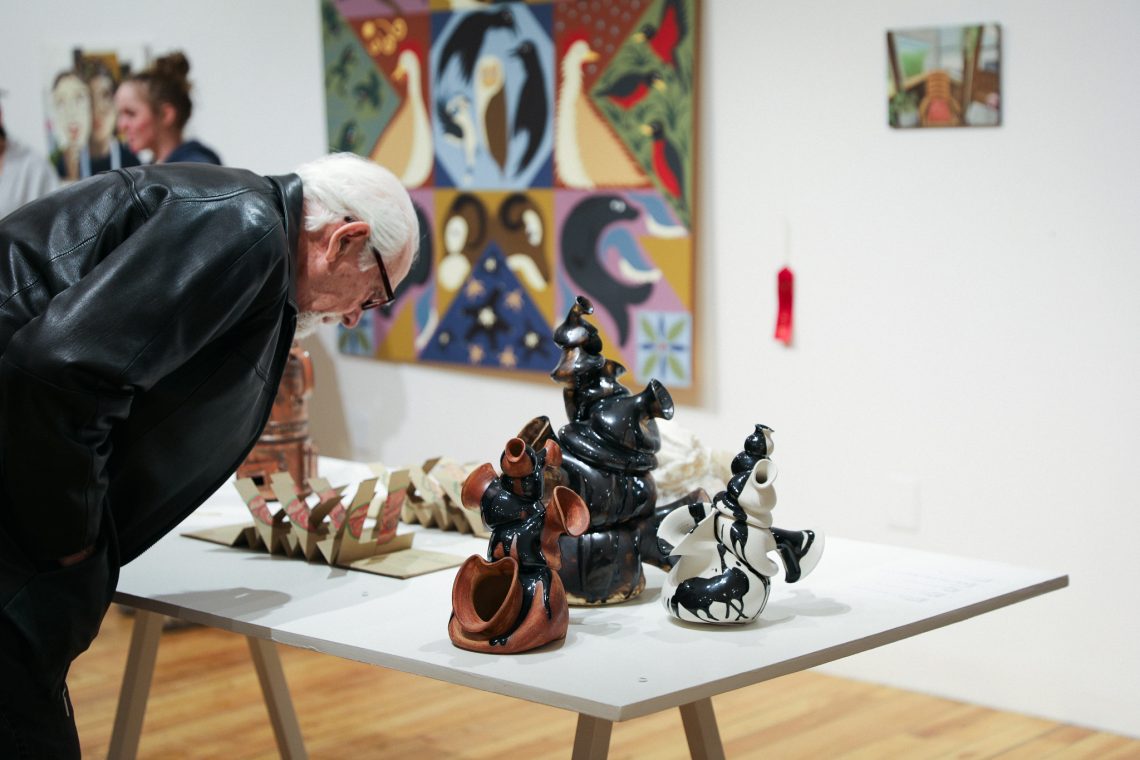 A visitor examines a piece of student artwork on a table at the USM Gorham Art Gallery during the 2026 Juried Student Art Exhibition.