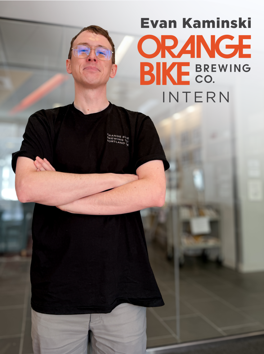 Evan Kaminski '26 stands for a photo op next to a rendered in Orange Bike Brewing Company Logo indicating his internship with them.