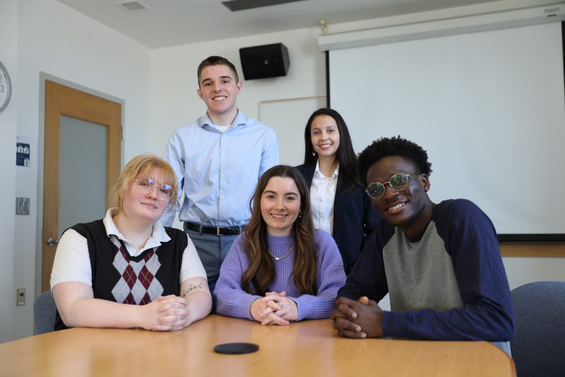 Five Forum on American Democracy scholars smile at the camera, gathered around a table—some seated and some standing—during a group photo.