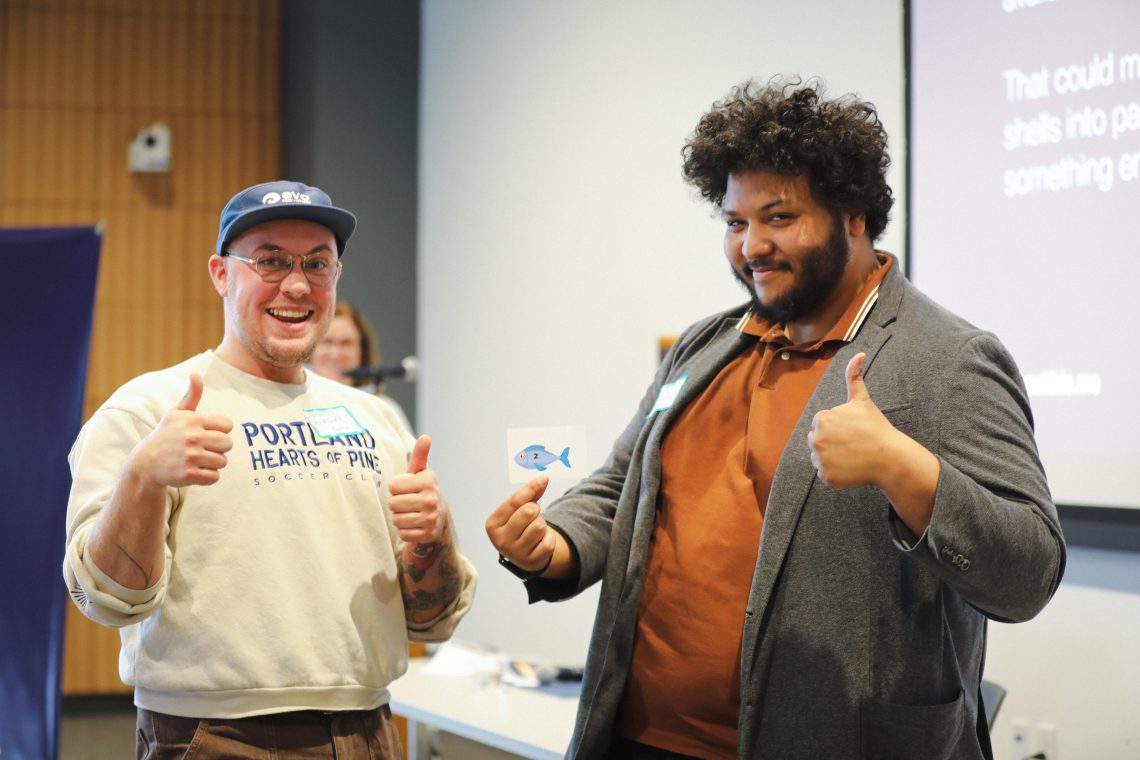 Team of students smile and give thumbs up while holding number card showing their presentation order
