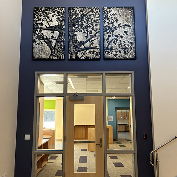 Photo of triptych woodcut of tree with children sitting in branches installed over doorway.