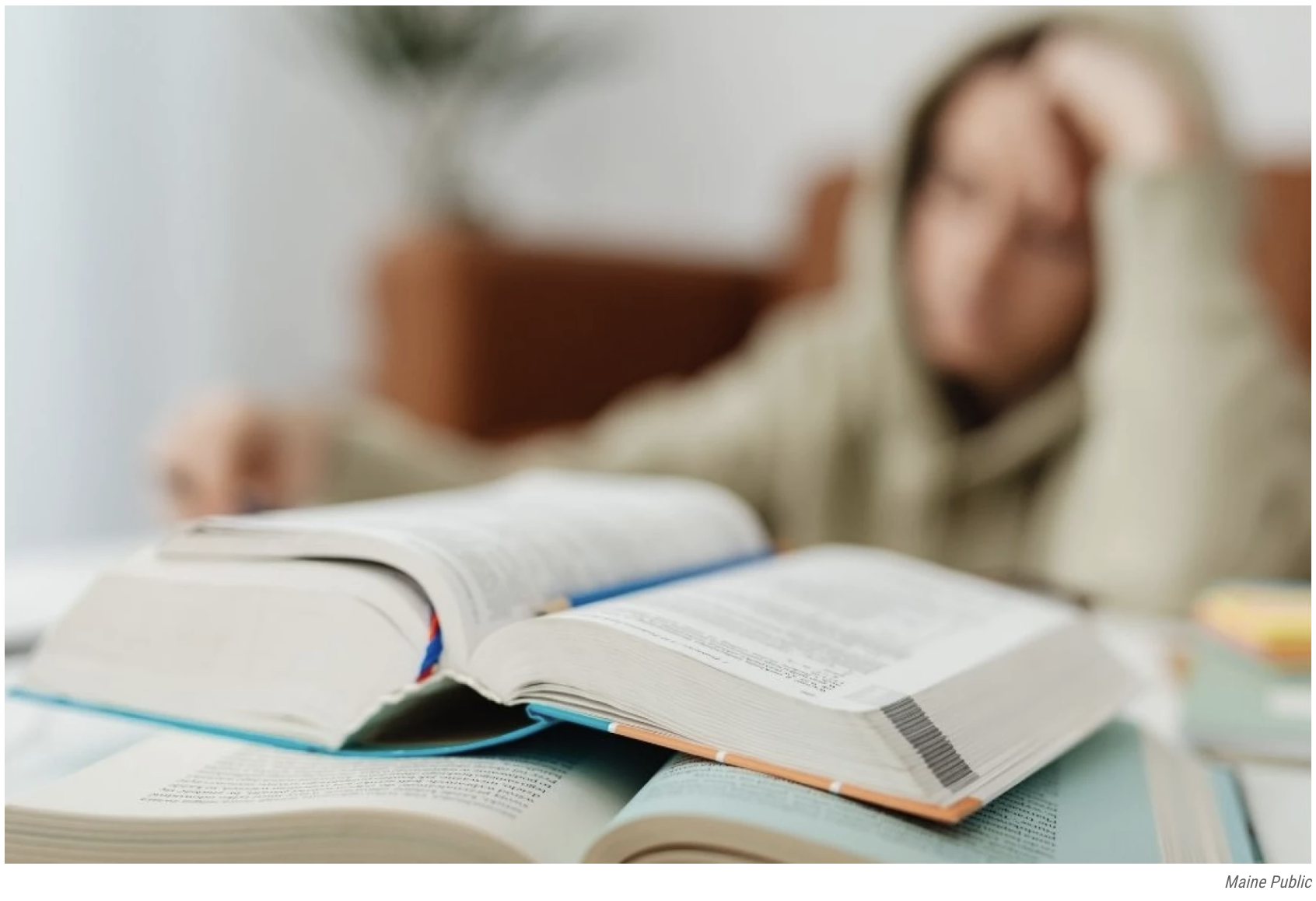 Open textbook on table with student in background studying.