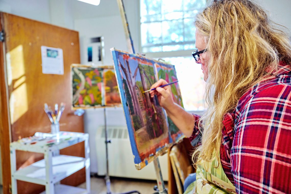 Student painting a colorful artwork in a light-filled studio space.