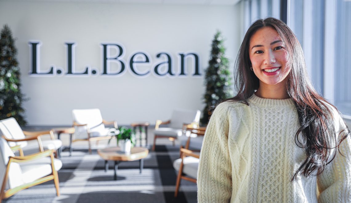 Mandy Ho smiles for the camera in a naturally lit room, with L.L.Bean on the wall in the background.
