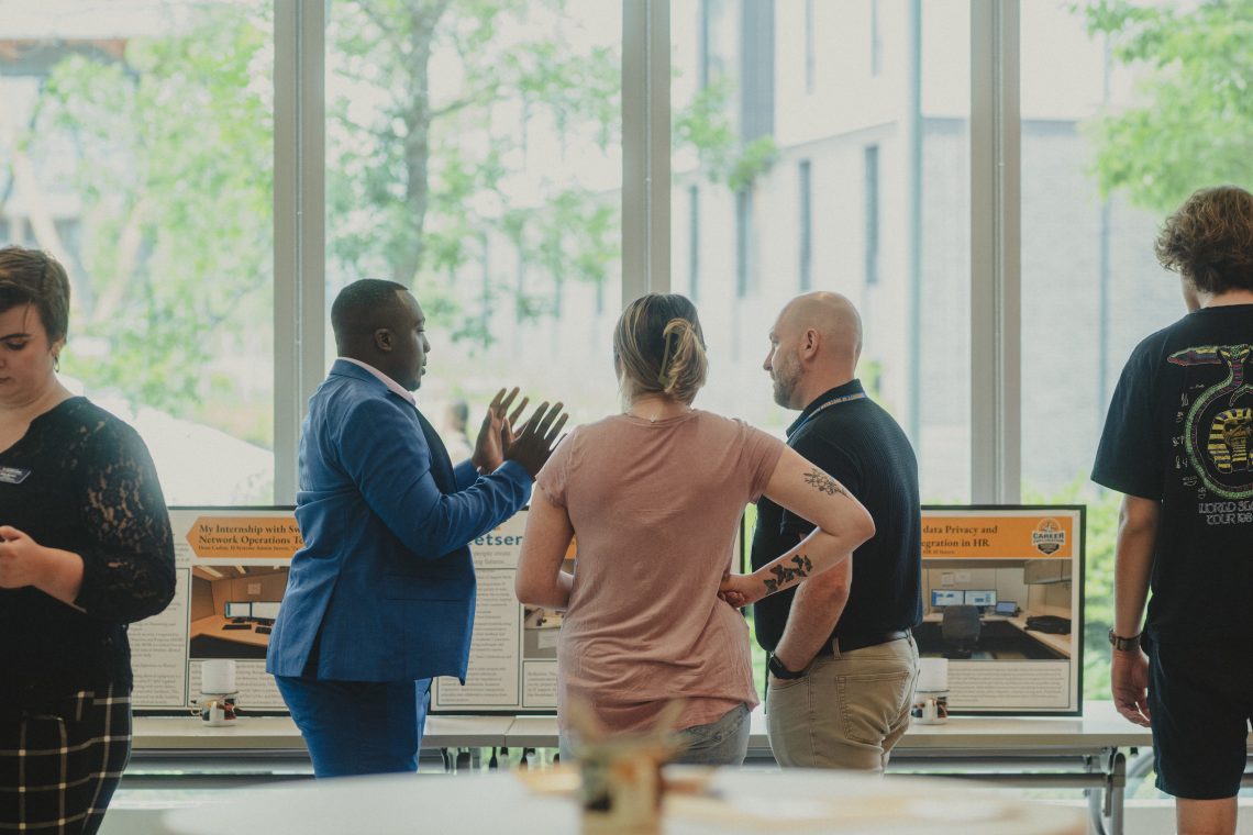Career Exploration Internship Program Poster Exhibition indoors, posters in view, with large windows in the background and people chatting near posters.