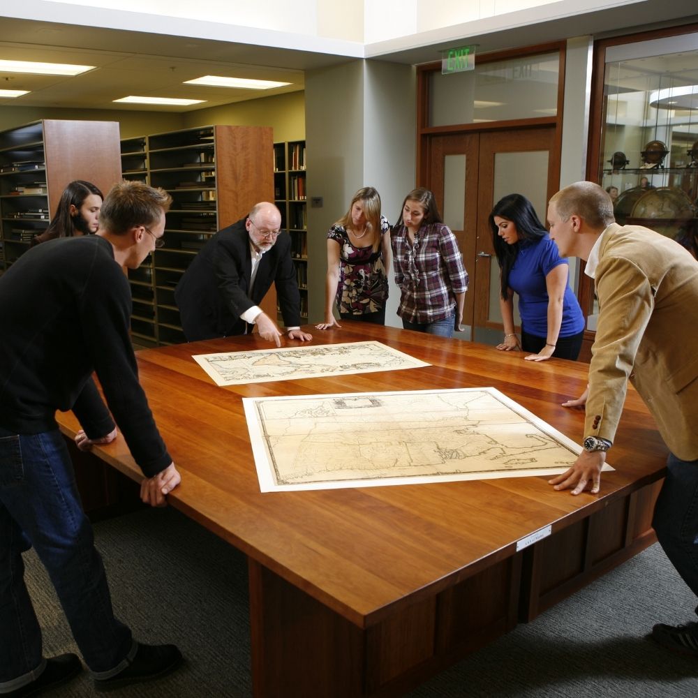 Professor reviewing replica historic maps in the Osher Map Library with students.