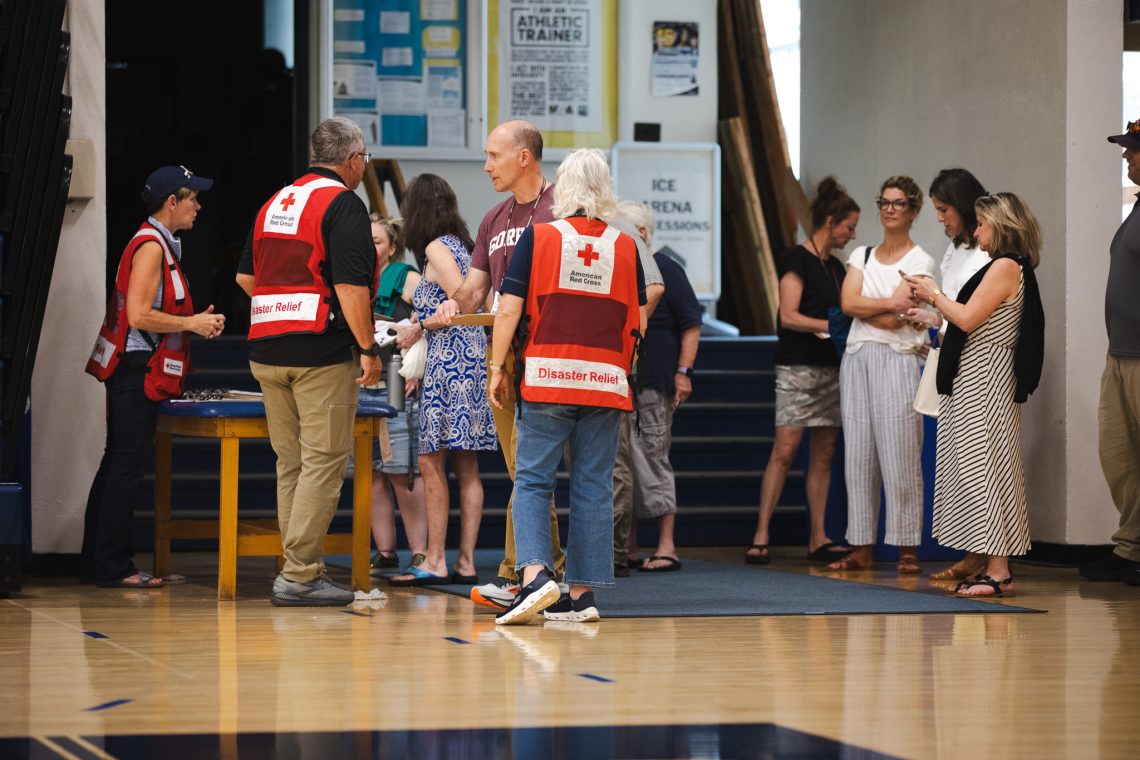 Red Cross Disaster Relief volunteers in red vests talk with school staff and community members inside a gymnasium during USM's school reunification exercise.