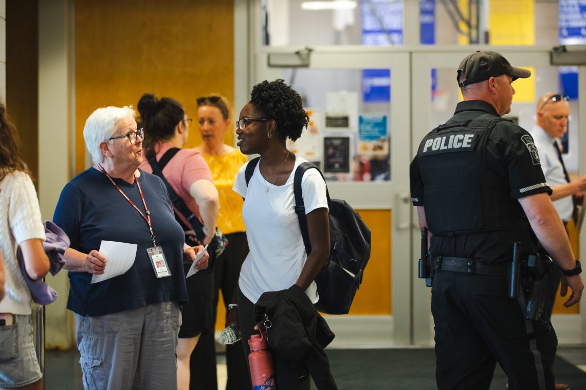 A student speaks with a Gorham Schools staff member near the building entrance as a police officer looks on during USM's reunification exercise.