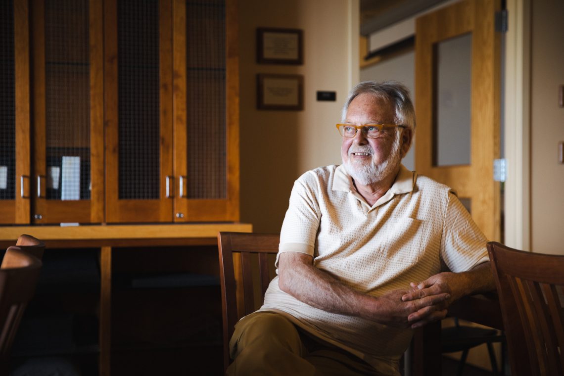 Steve Bull, co-founder of the Wilde Stein Club and the Maine Gay Task Force, sits in a chair at USM Special Collections, smiling and looking off to the side.