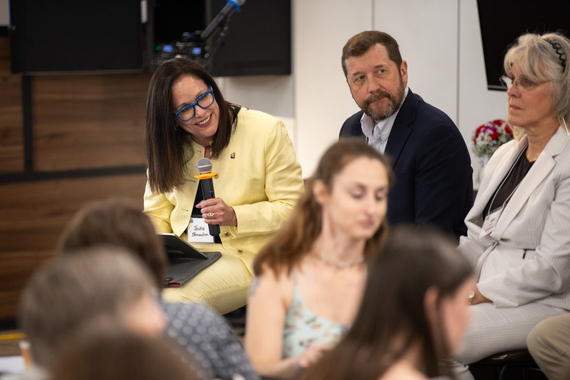 USM President Jacqueline Edmondson holds a microphone while moderating a pannel.