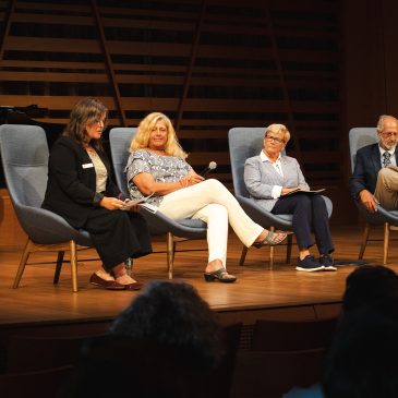 Mollie Cashwell speaks into a microphone during a panel discussion with NEA Chairman Mary Anne Carter, Congresswoman Chellie Pingree, and Maine Arts Commission Chair Bob Keyes, seated left to right, at USM's Crewe Center for the Arts.