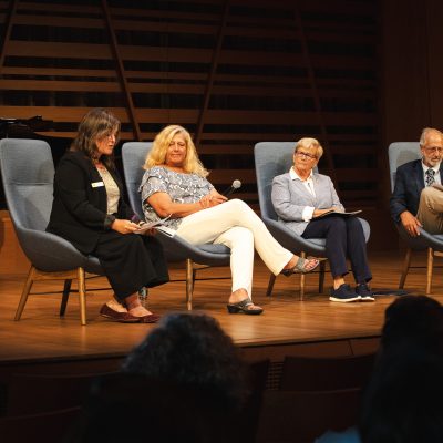 Mollie Cashwell speaks into a microphone during a panel discussion with NEA Chairman Mary Anne Carter, Congresswoman Chellie Pingree, and Maine Arts Commission Chair Bob Keyes, seated left to right, at USM's Crewe Center for the Arts.