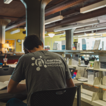 Student sitting in USM library with a Learning Assistant Program tshirt
