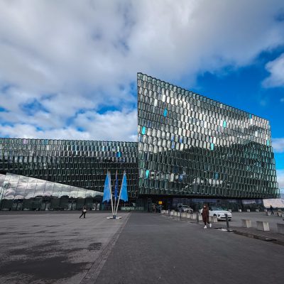 The glass exterior of Harpa in Reykjavik, Iceland, the venue for the Arctic Circle Assembly, with blue flags out front.