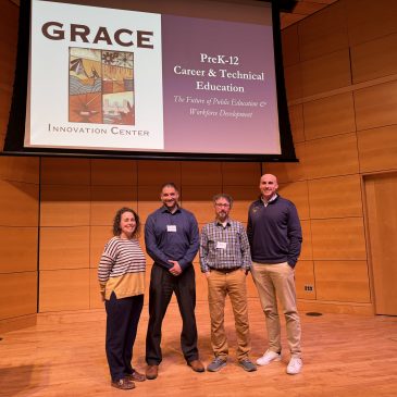 4 people standing on a stage with a projector screen behind them