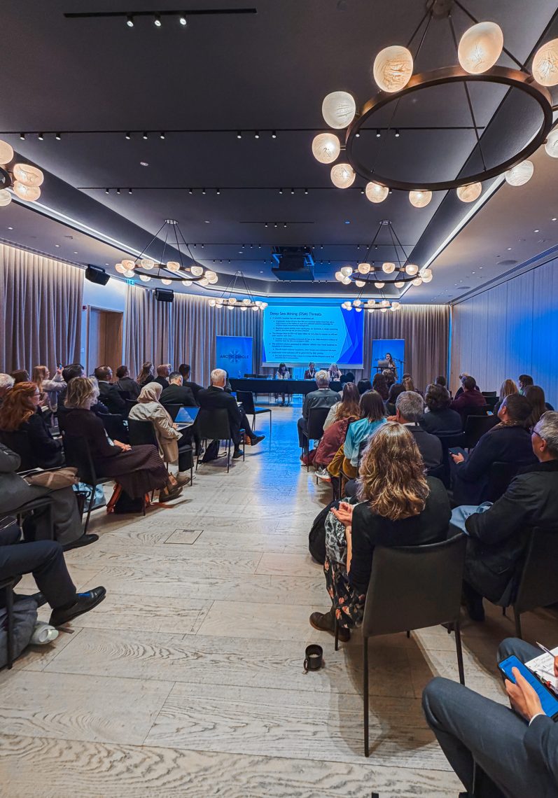 A full room of attendees listens to a panel on deep-sea mining at the Arctic Circle Assembly, with a slide titled “Deep-Sea Mining (DSM) Threats” projected at the front.