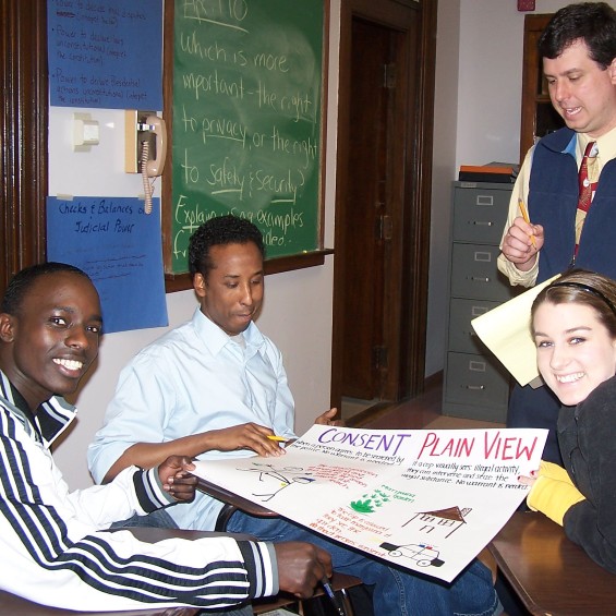 High school teacher standing and students at desk with poster