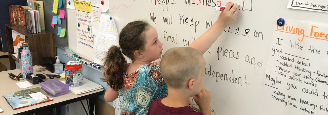 Two elementary students working at whiteboard in classroom