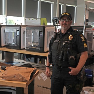 Sgt. Ben Moreland waits while a 3D printer at the MIST Lab makes a locking device that will attach a body-worn camera to his MOLLE vest.