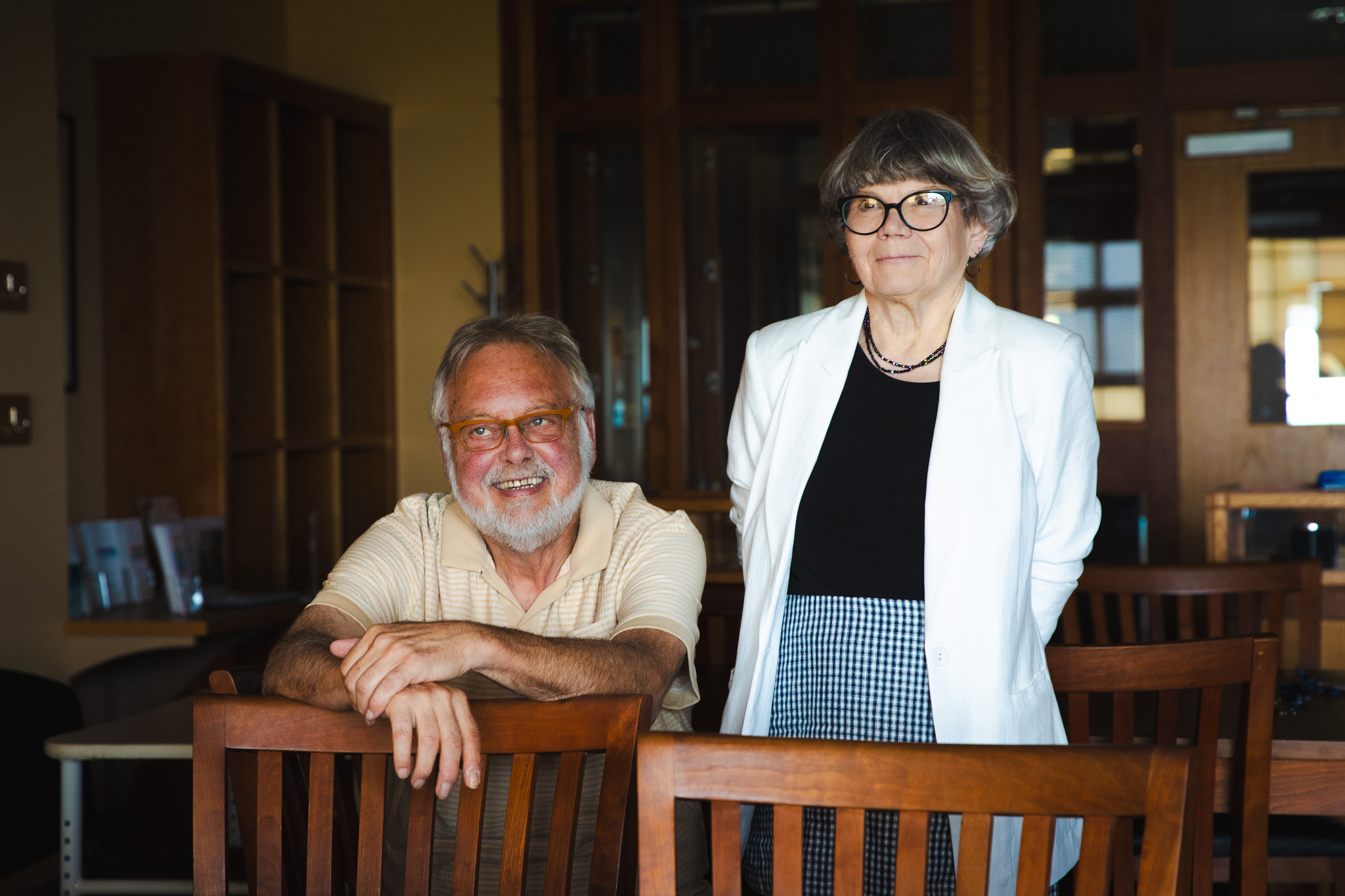 Steve Bull and Susie Bock pose together at USM Special Collections, Bull seated and smiling with his arms resting on a chair, Bock standing beside him.