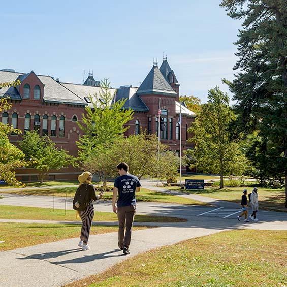Two students, deep in conversation, walking toward Corthell Hall on our Gorham campus. Another two students cross their path in the distance ahead.