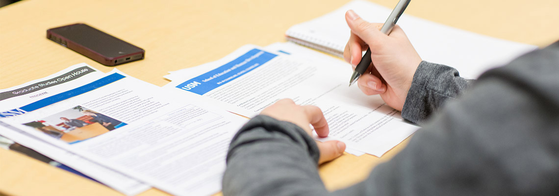 A student sits at a table and writes on a stack of papers.