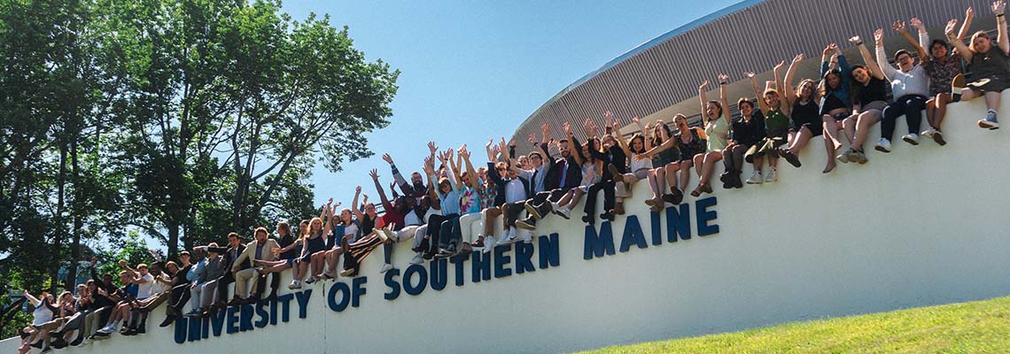 Cheering students sitting on the Gorham campus USM wall.