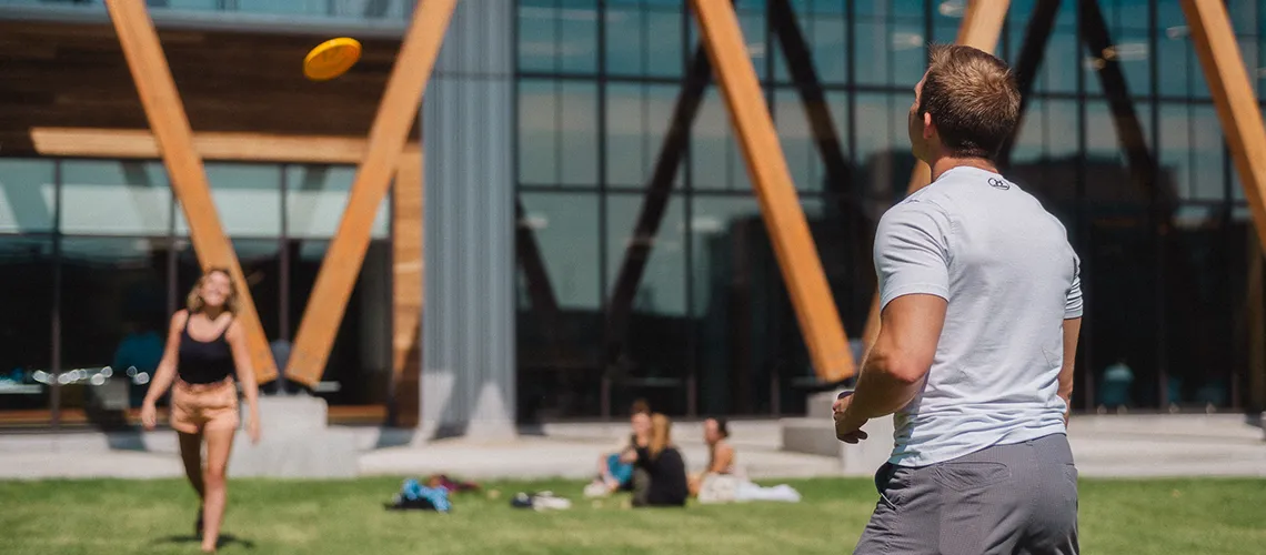 Students dressed in shorts play frisbee on the Bean Green on a sunny day.